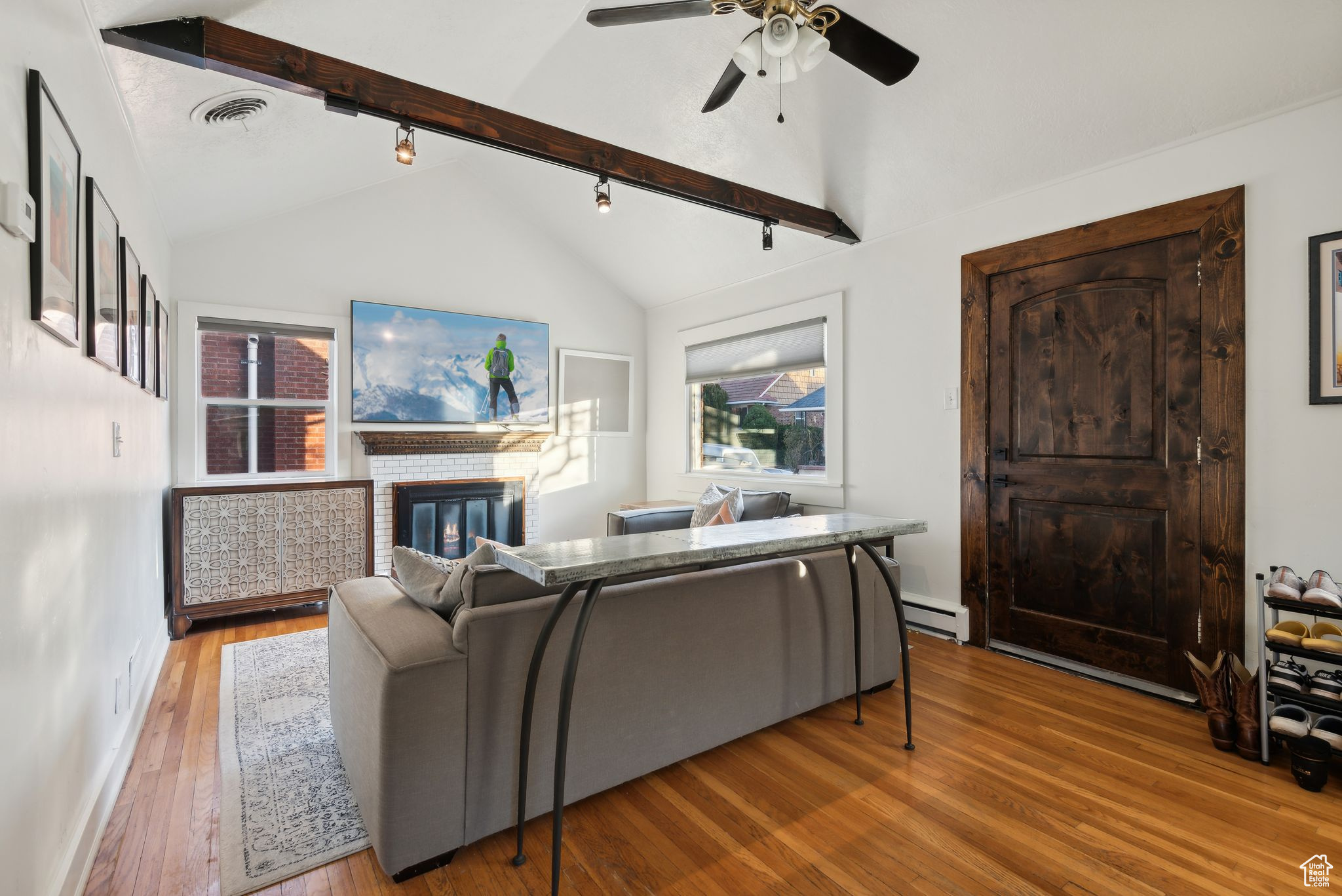 Living room featuring lofted ceiling with beams, rail lighting, hardwood / wood-style flooring, a fireplace, and a baseboard radiator