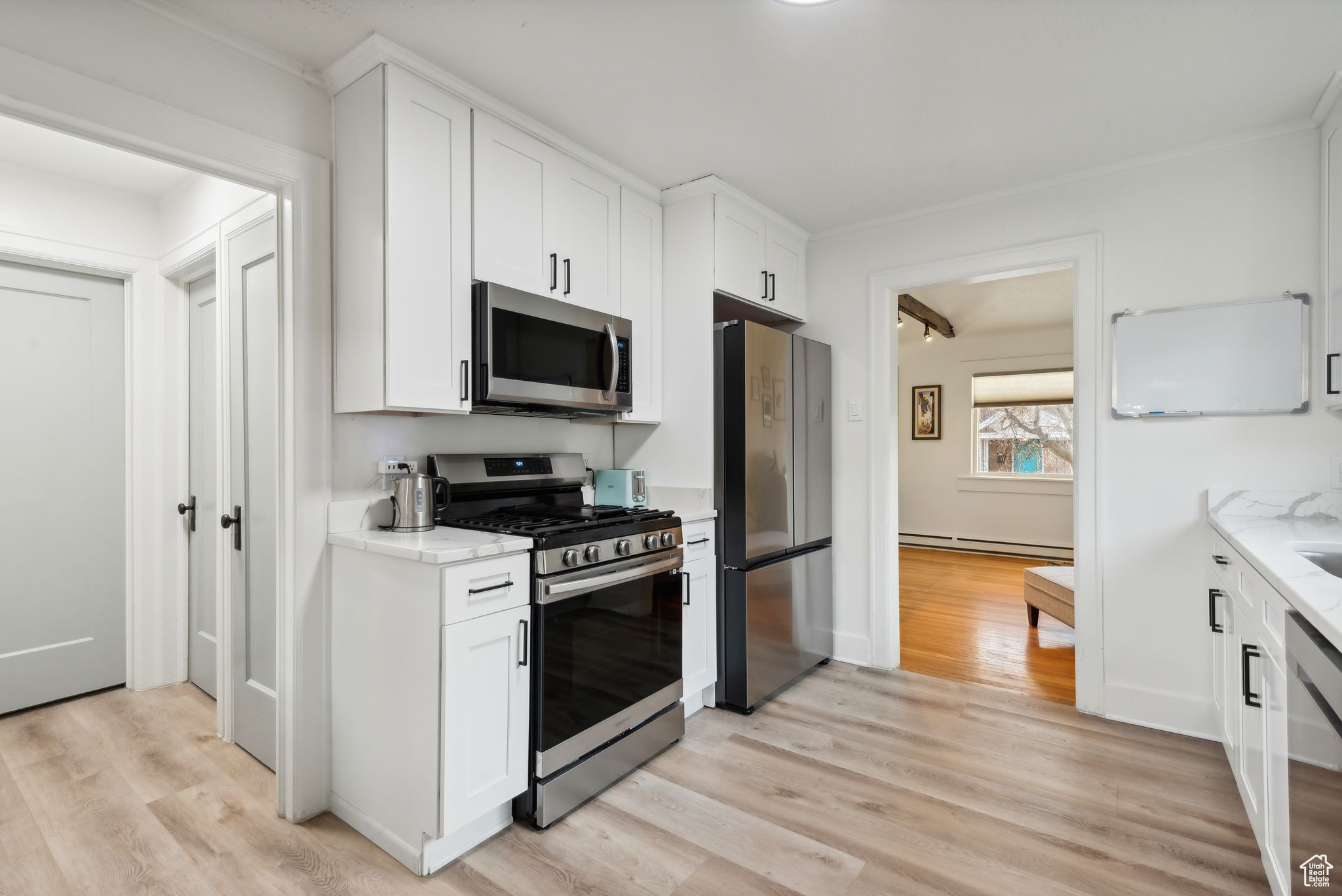 Kitchen featuring light stone counters, white cabinets, stainless steel appliances, and light hardwood / wood-style floors