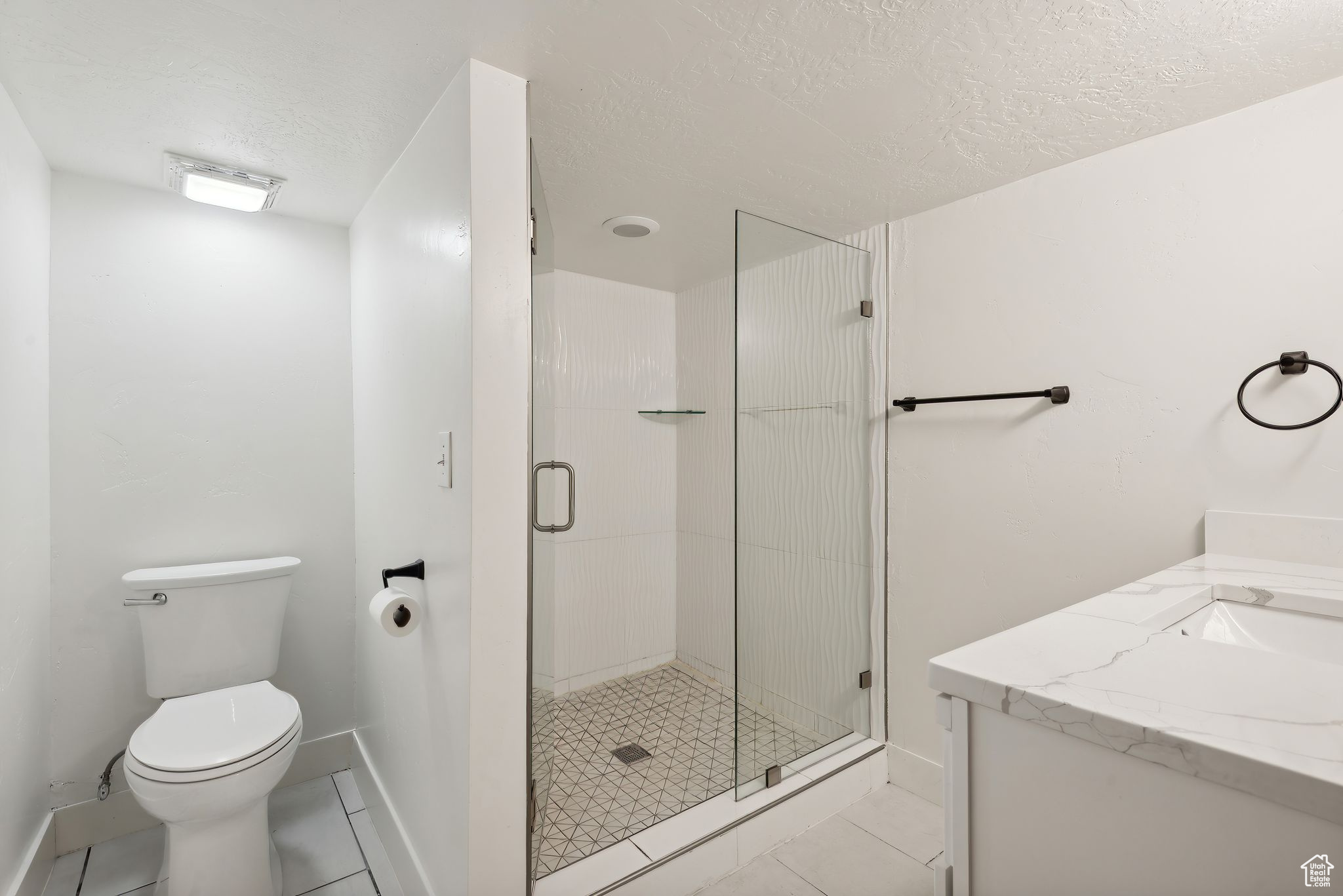 Bathroom featuring tile patterned floors, a textured ceiling, an enclosed shower, toilet, and vanity