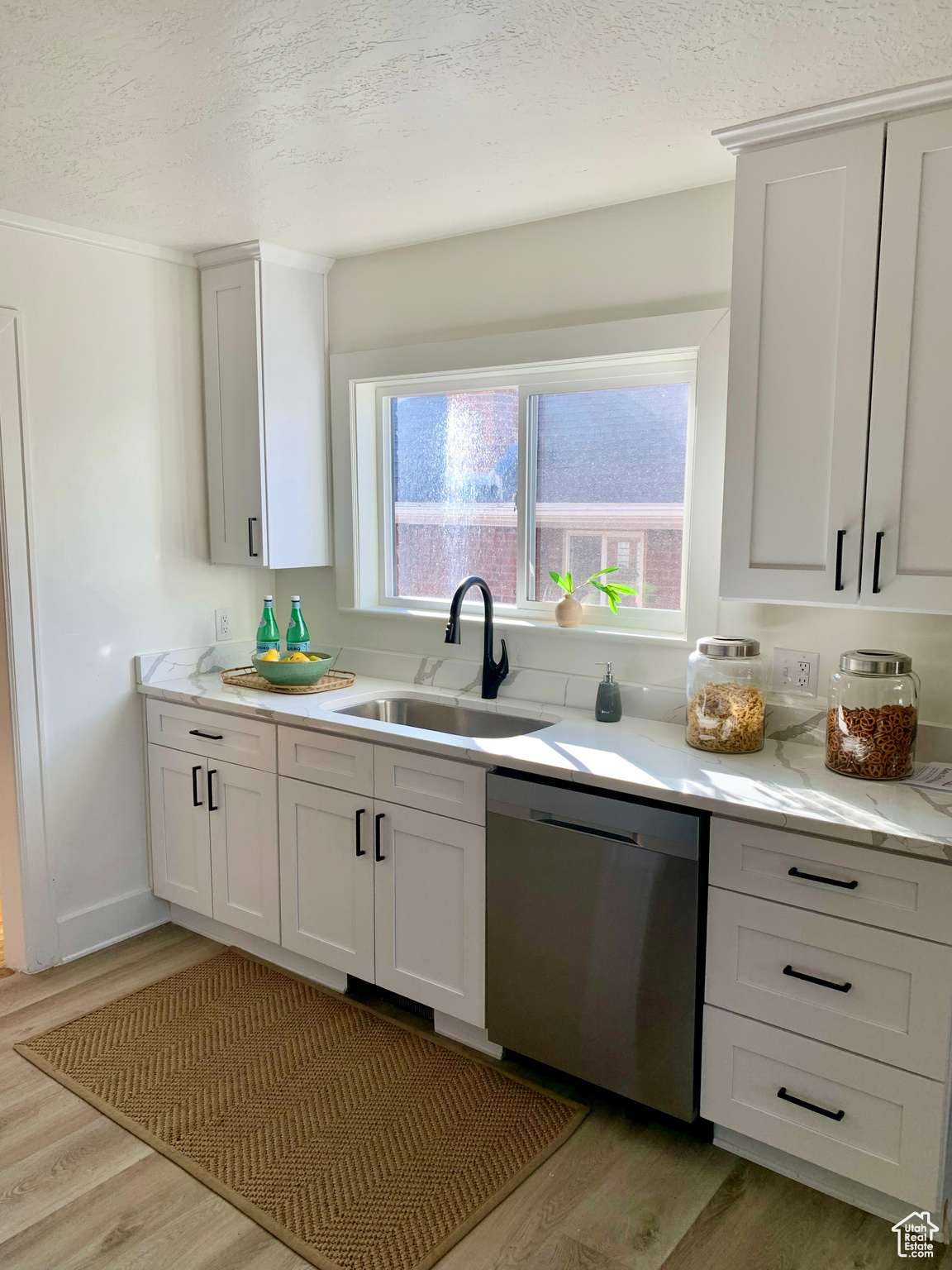 Kitchen featuring dishwasher, white cabinets, light wood-type flooring, and sink