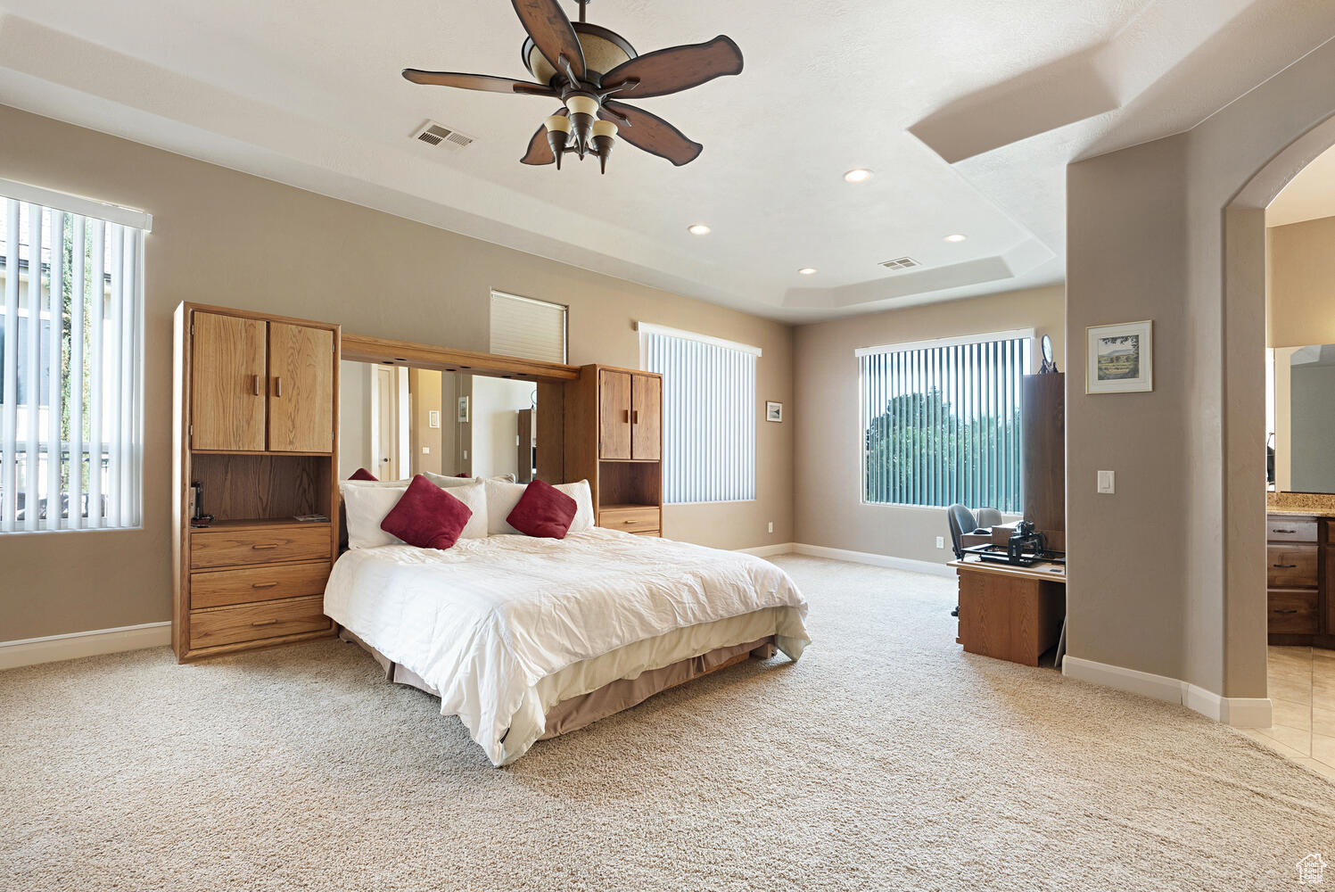 Bedroom featuring multiple windows, light carpet, connected bathroom, and ceiling fan