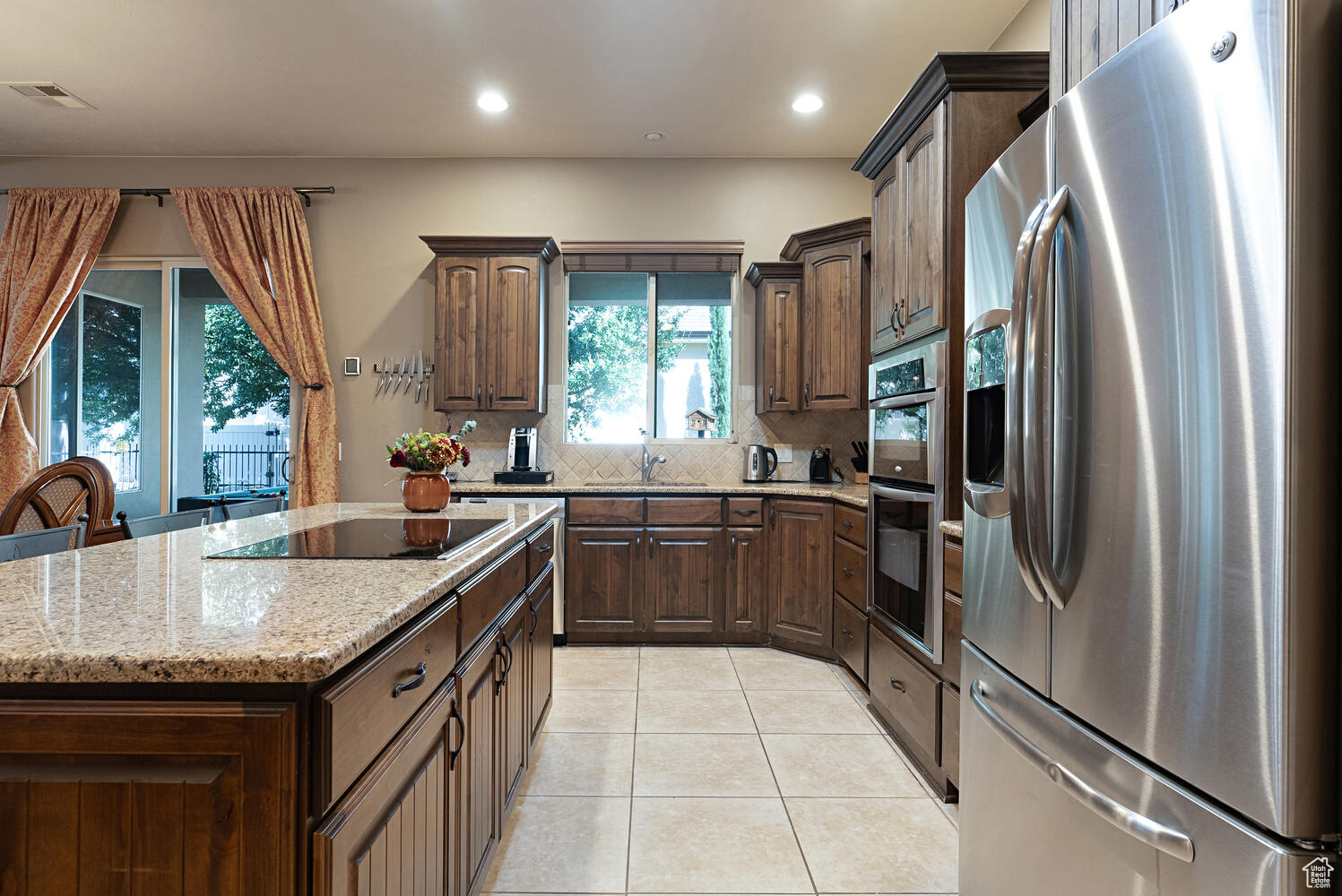 Kitchen with a center island, sink, stainless steel appliances, backsplash, and light tile patterned flooring