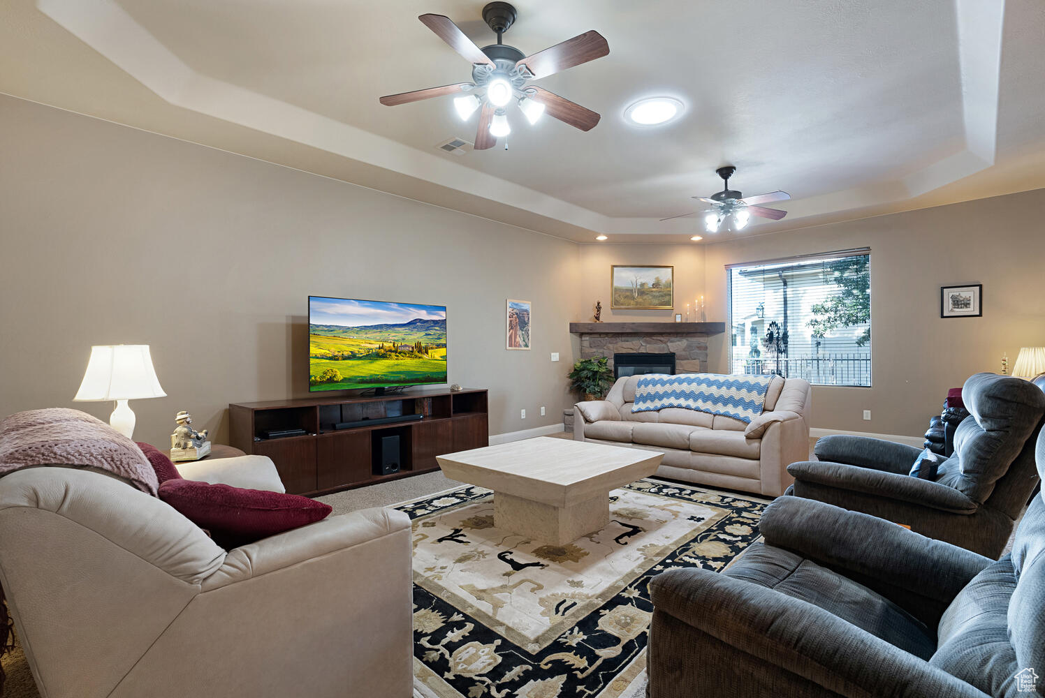 Living room featuring ceiling fan, a raised ceiling, and a fireplace