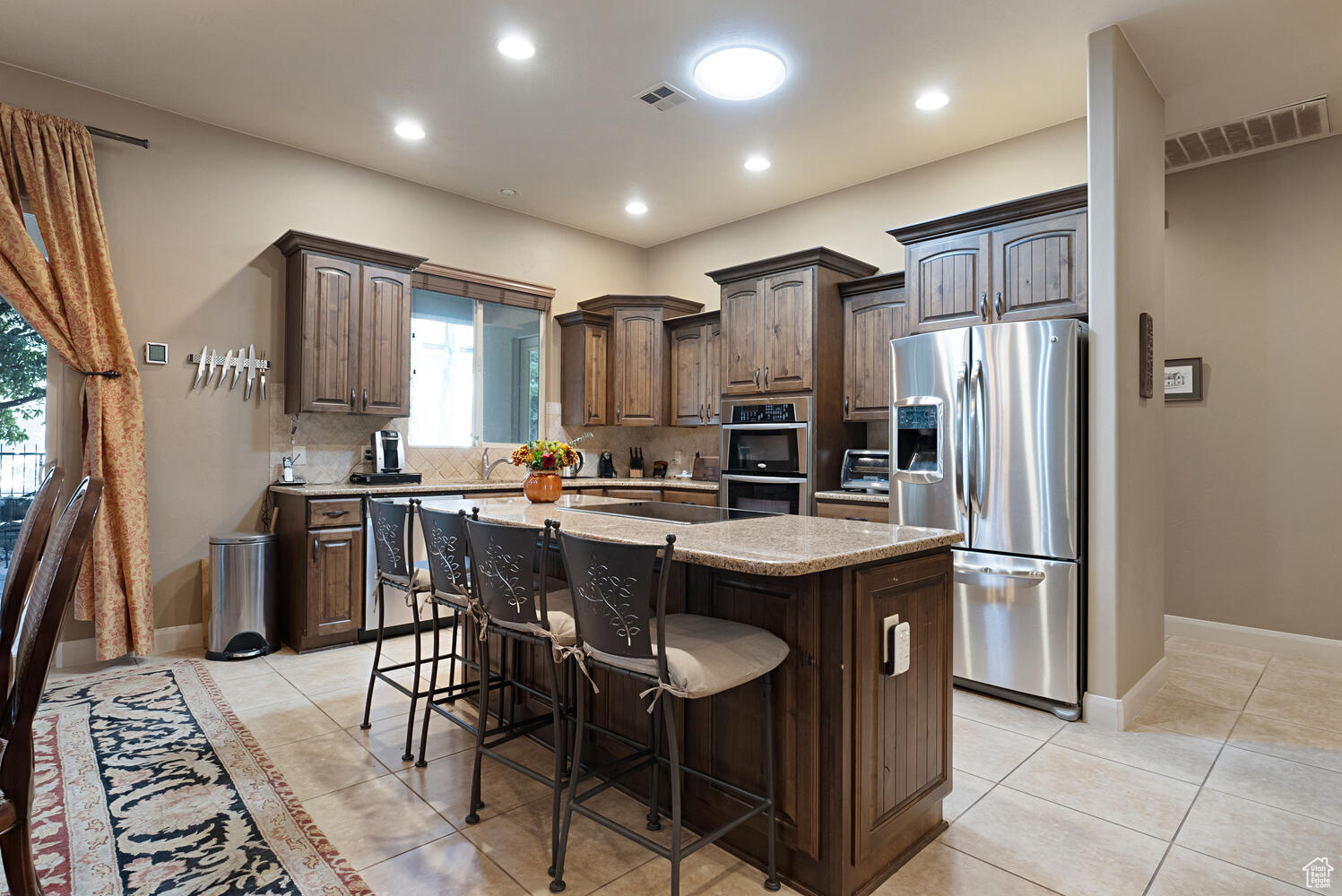 Kitchen with a breakfast bar, a center island, decorative backsplash, light tile patterned floors, and stainless steel appliances