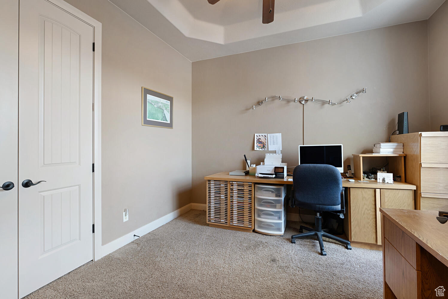 Carpeted home office featuring ceiling fan and a tray ceiling