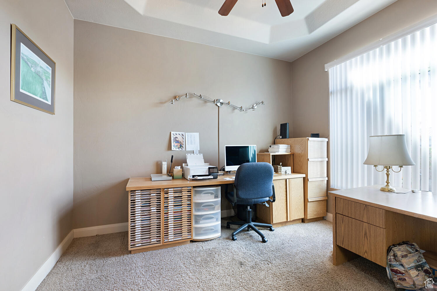 Home office featuring a raised ceiling, ceiling fan, and light colored carpet