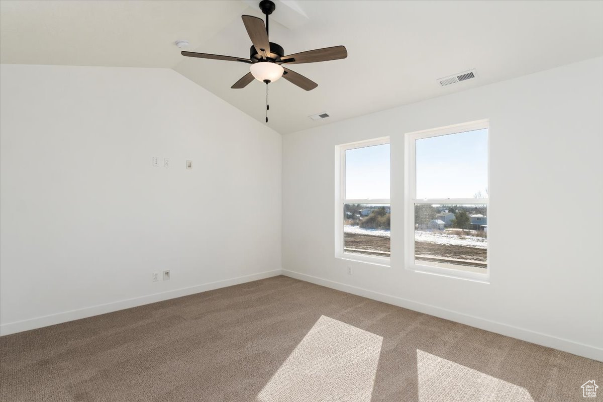 Carpeted spare room featuring ceiling fan and vaulted ceiling