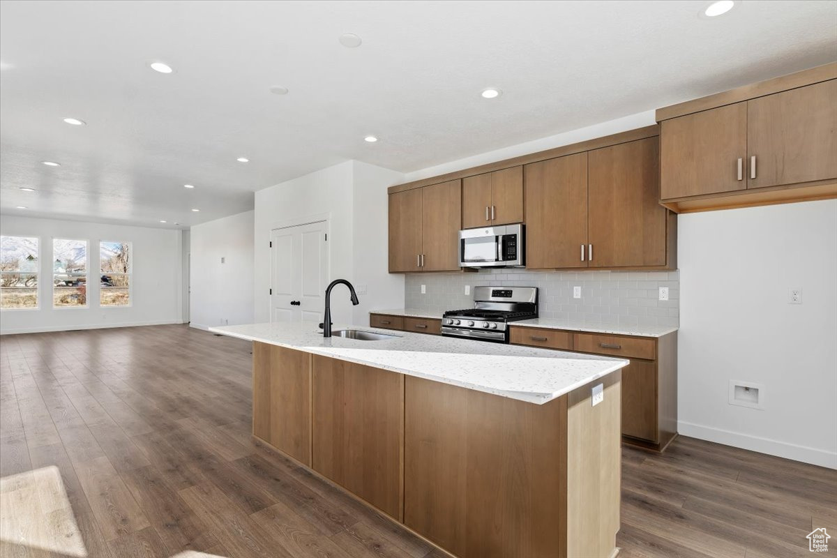 Kitchen with decorative backsplash, appliances with stainless steel finishes, a center island with sink, and sink