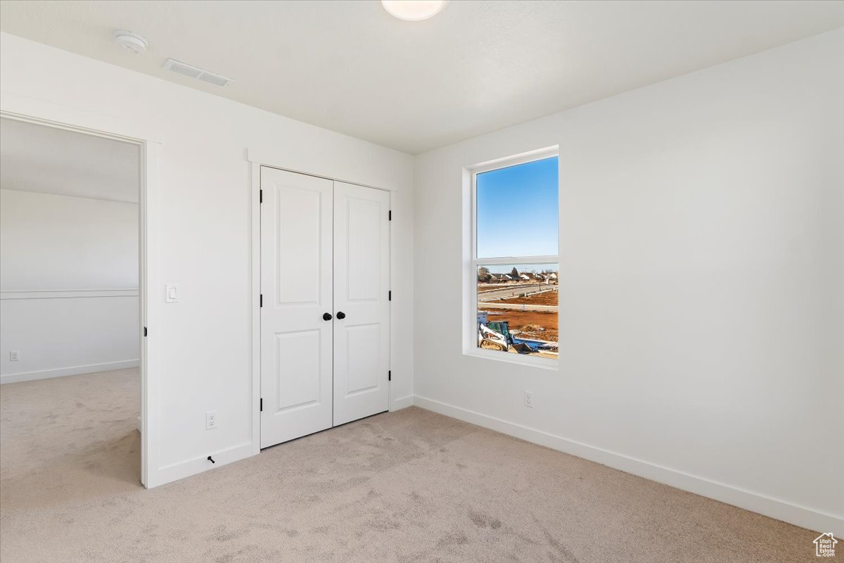 Unfurnished bedroom with light carpet and a closet