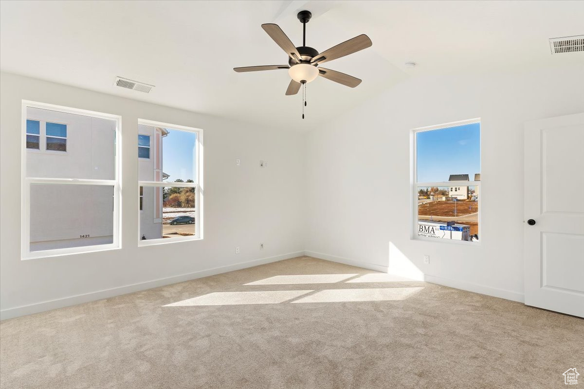 Carpeted spare room featuring ceiling fan and vaulted ceiling