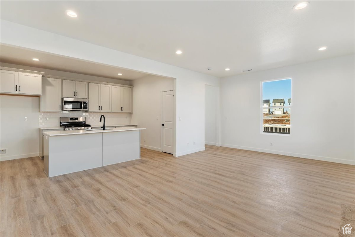 Kitchen featuring appliances with stainless steel finishes, backsplash, a kitchen island with sink, light hardwood / wood-style floors, and white cabinetry