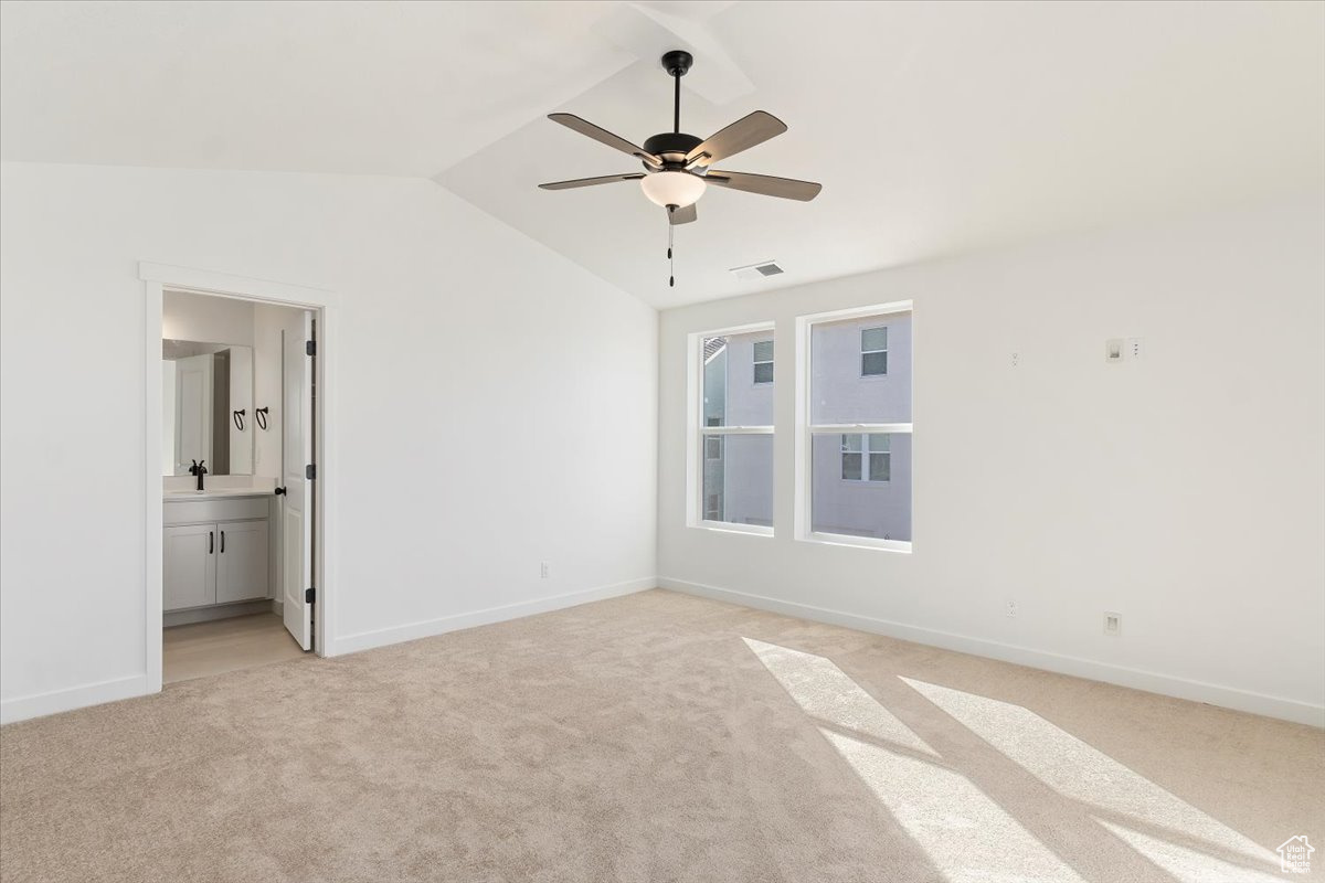 Unfurnished bedroom featuring ensuite bath, ceiling fan, sink, light colored carpet, and vaulted ceiling