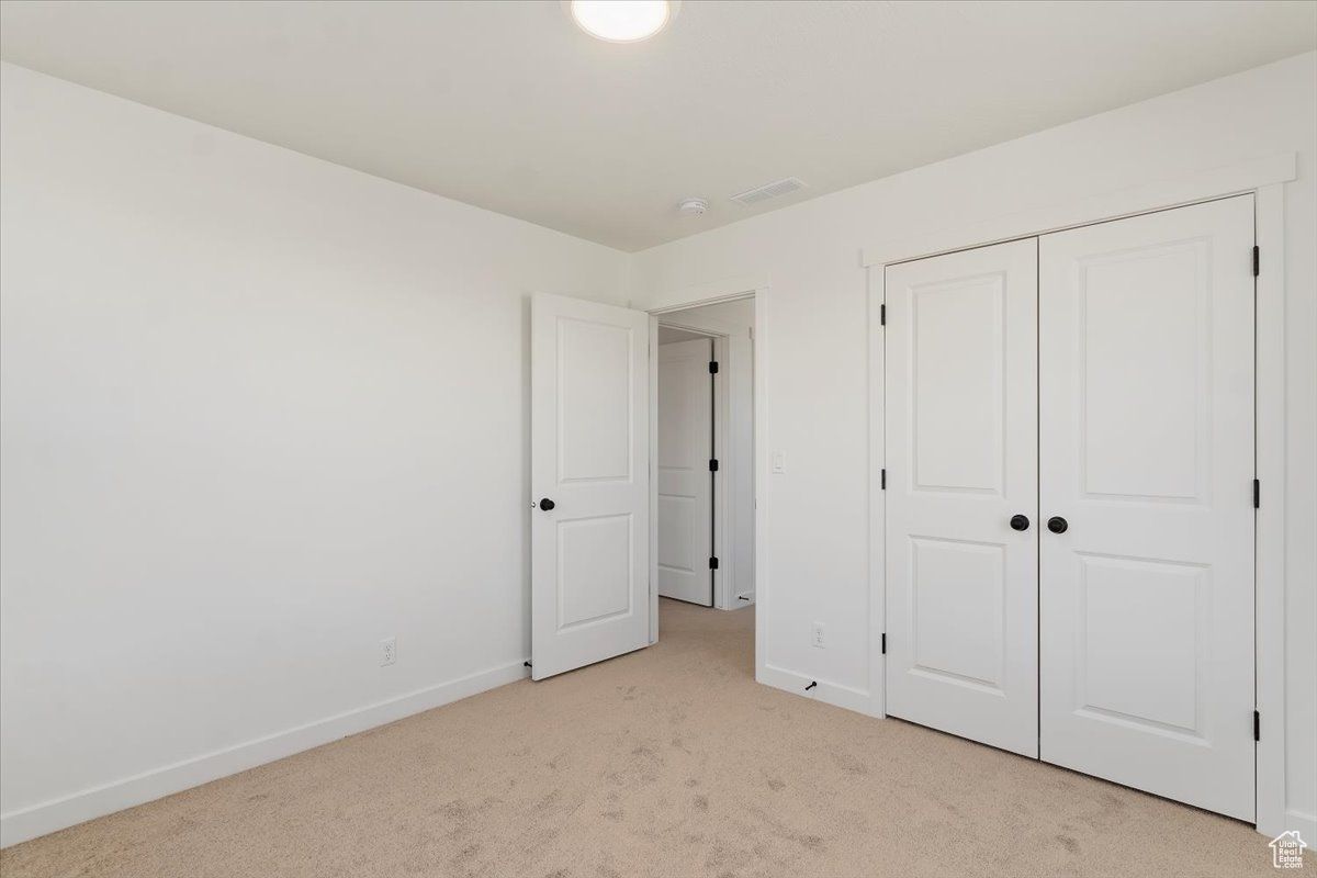 Unfurnished bedroom with light colored carpet and a closet