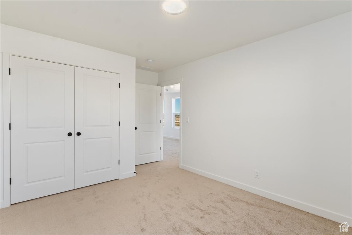 Unfurnished bedroom featuring light carpet and a closet