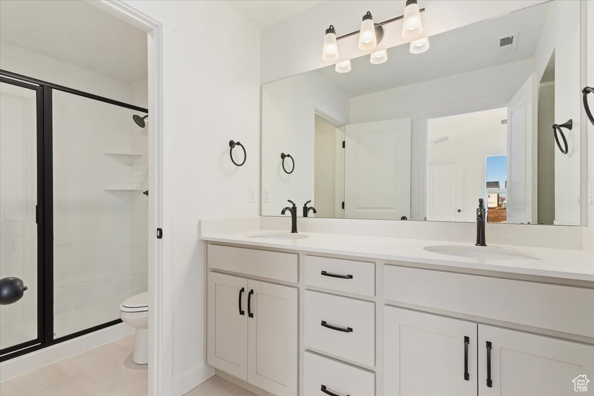 Bathroom featuring tile patterned flooring, vanity, toilet, and a shower with shower door