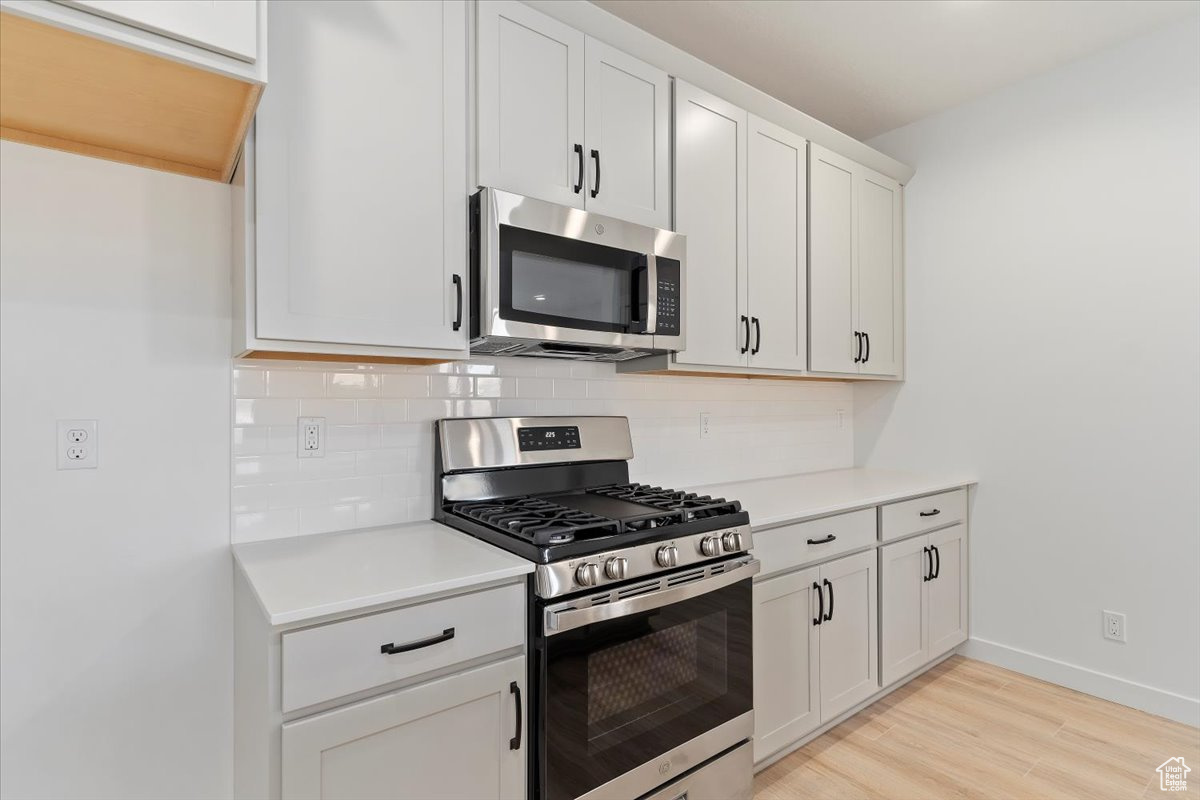 Kitchen featuring backsplash, white cabinetry, light hardwood / wood-style flooring, and appliances with stainless steel finishes