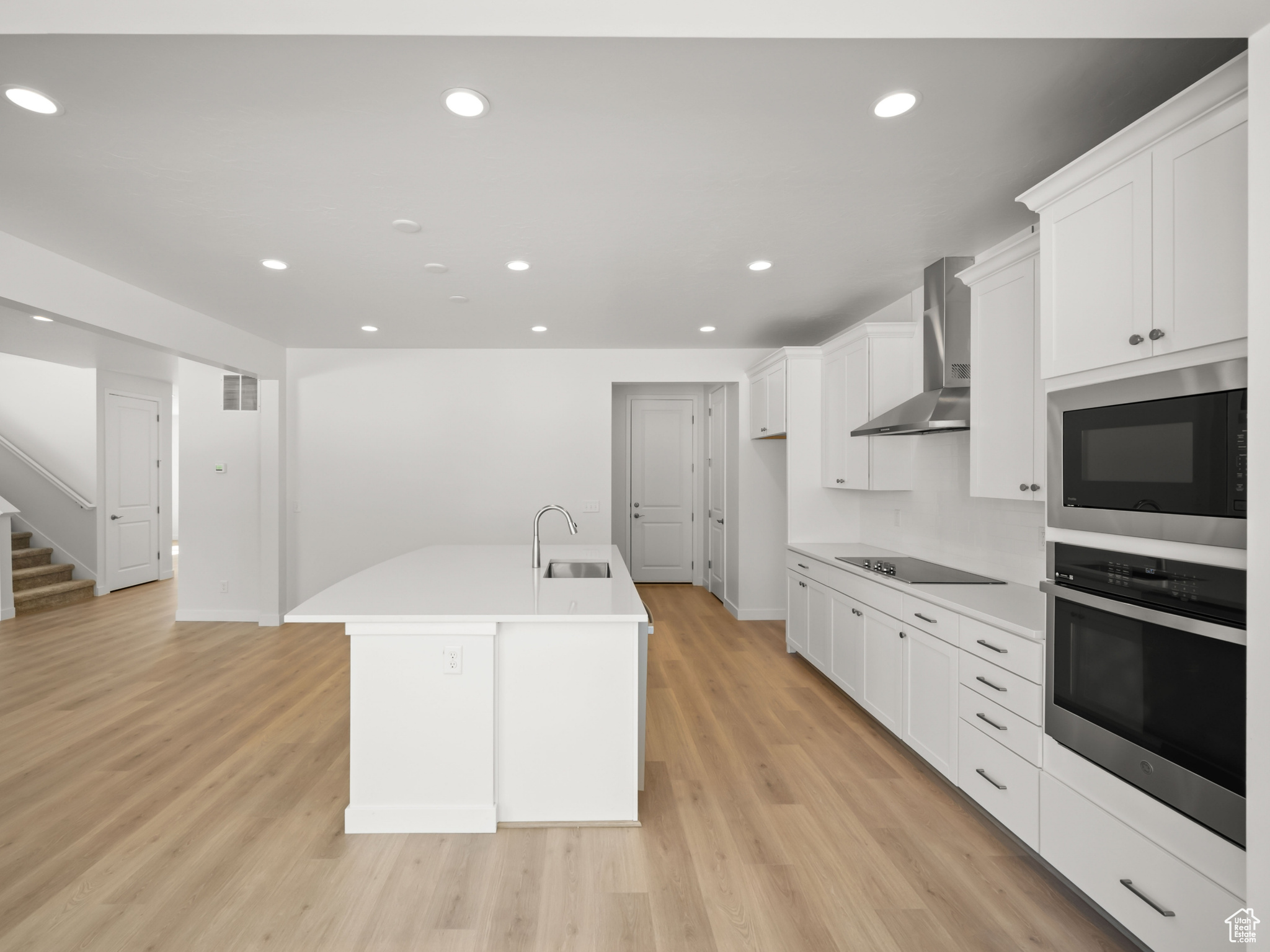 Kitchen with built in microwave, stainless steel oven, sink, wall chimney range hood, and a kitchen island with sink