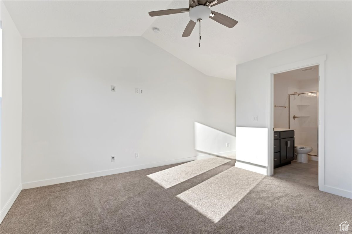 Unfurnished bedroom with carpet floors, ensuite bath, vaulted ceiling, and ceiling fan