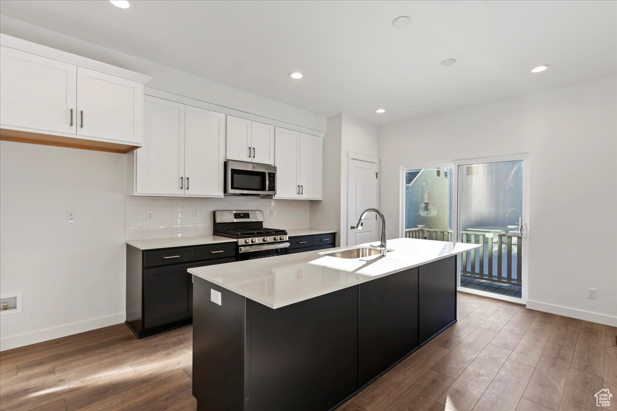 Kitchen featuring white cabinets, stainless steel appliances, a center island with sink, and sink