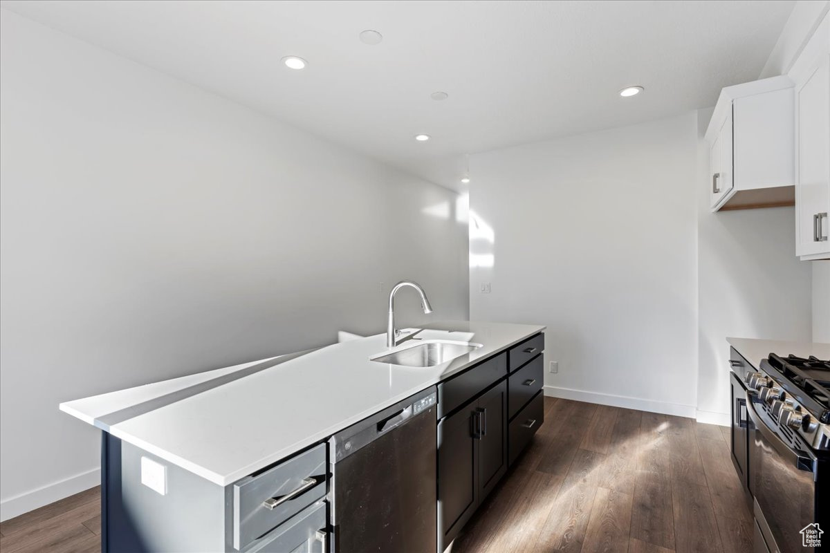 Kitchen with sink, dark hardwood / wood-style flooring, a kitchen island with sink, white cabinets, and appliances with stainless steel finishes