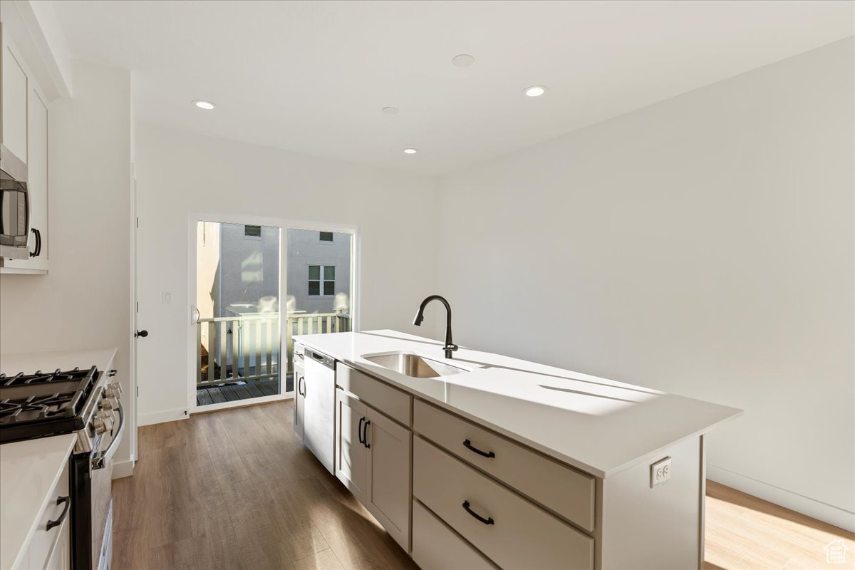 Kitchen with a kitchen island with sink, sink, hardwood / wood-style flooring, appliances with stainless steel finishes, and white cabinetry