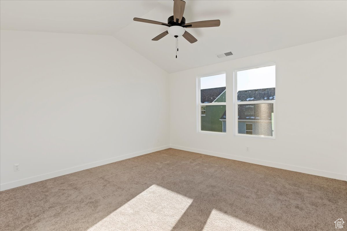 Empty room featuring carpet, ceiling fan, and vaulted ceiling