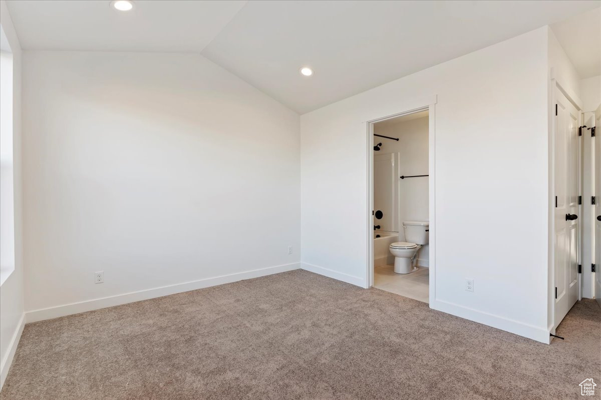 Unfurnished bedroom with light carpet, ensuite bathroom, and lofted ceiling