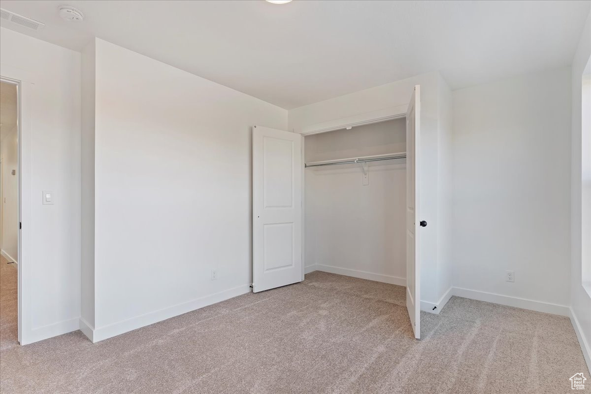 Unfurnished bedroom featuring light carpet and a closet