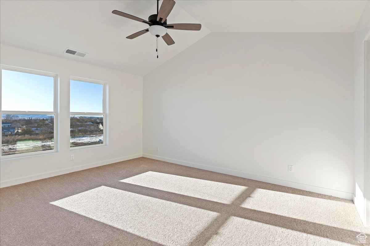 Empty room featuring carpet floors, vaulted ceiling, and ceiling fan