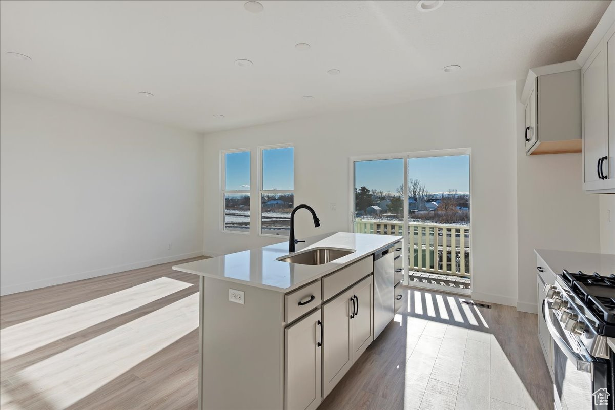 Kitchen with a kitchen island with sink, white cabinets, sink, appliances with stainless steel finishes, and light hardwood / wood-style floors