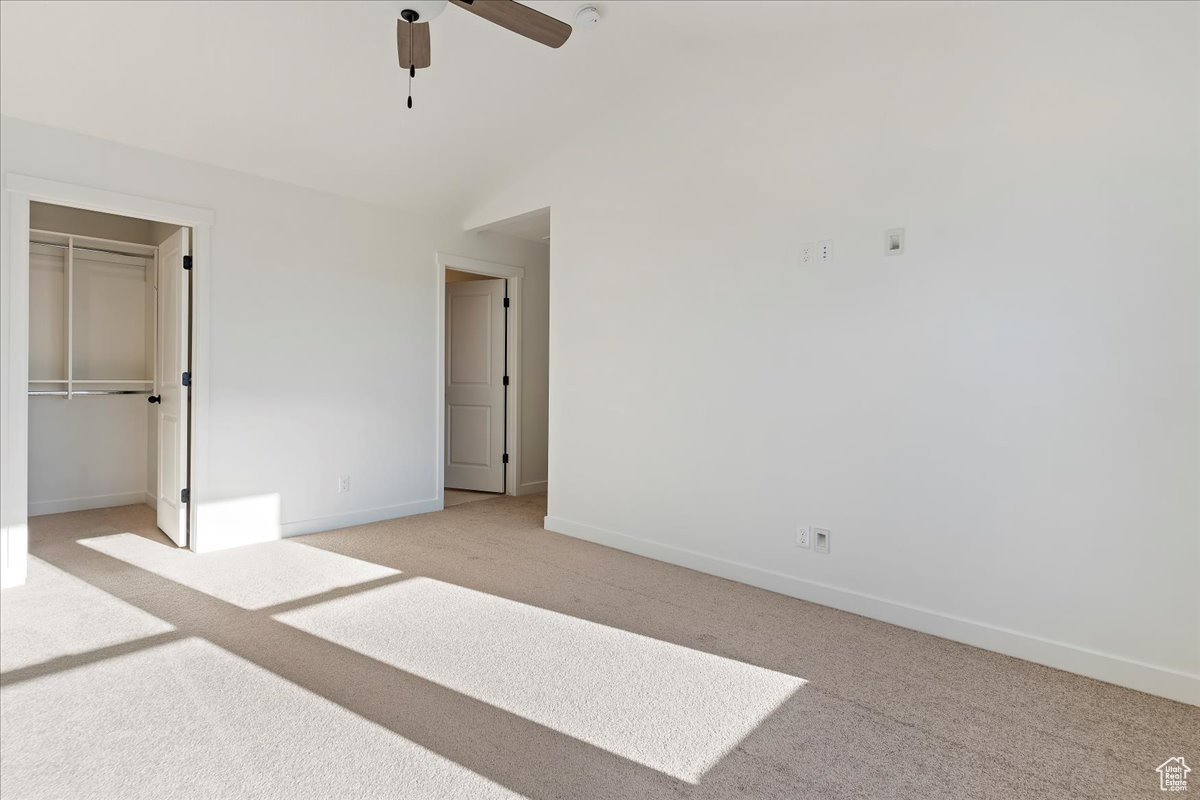 Unfurnished bedroom with ceiling fan, a closet, light carpet, and vaulted ceiling