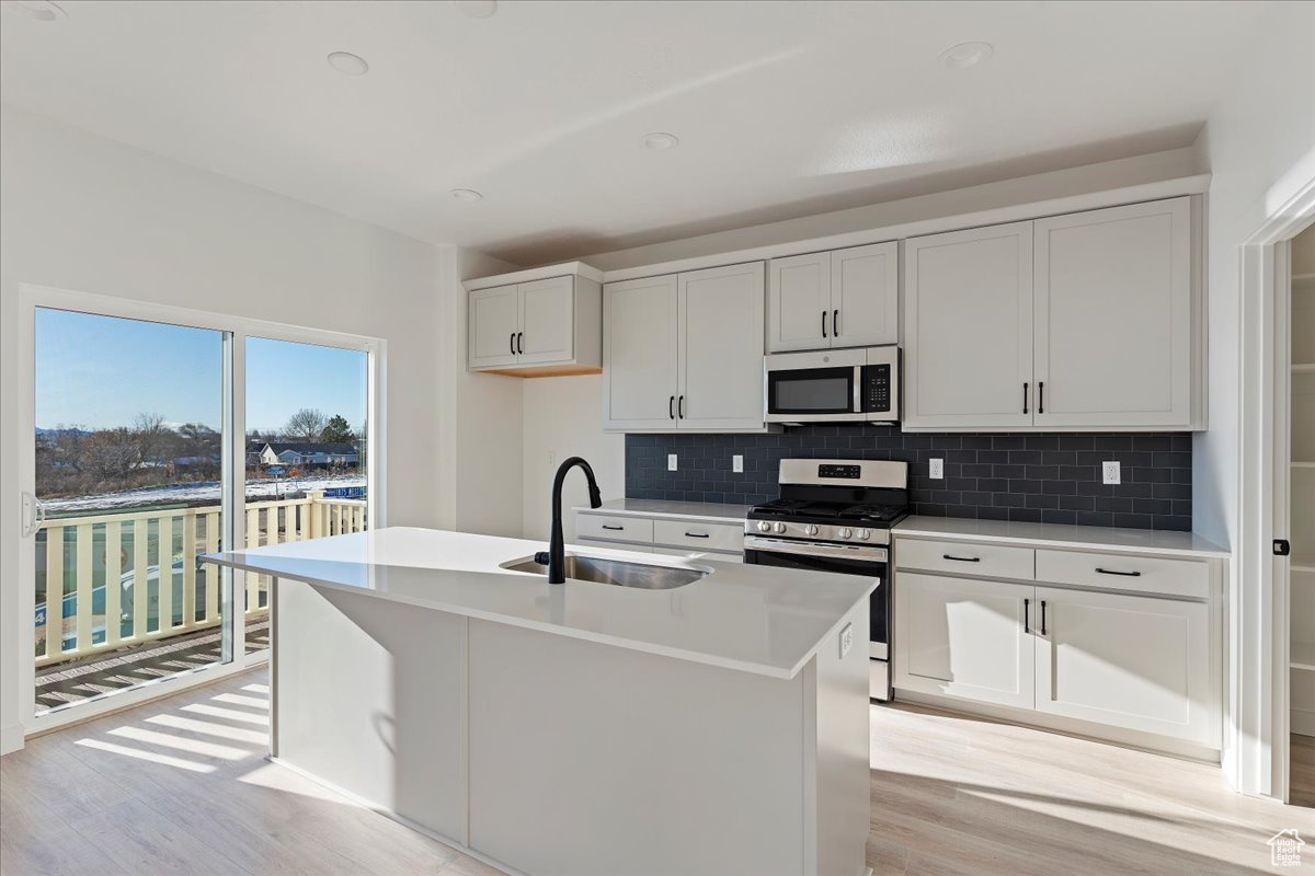 Kitchen featuring appliances with stainless steel finishes, tasteful backsplash, sink, a center island with sink, and white cabinets