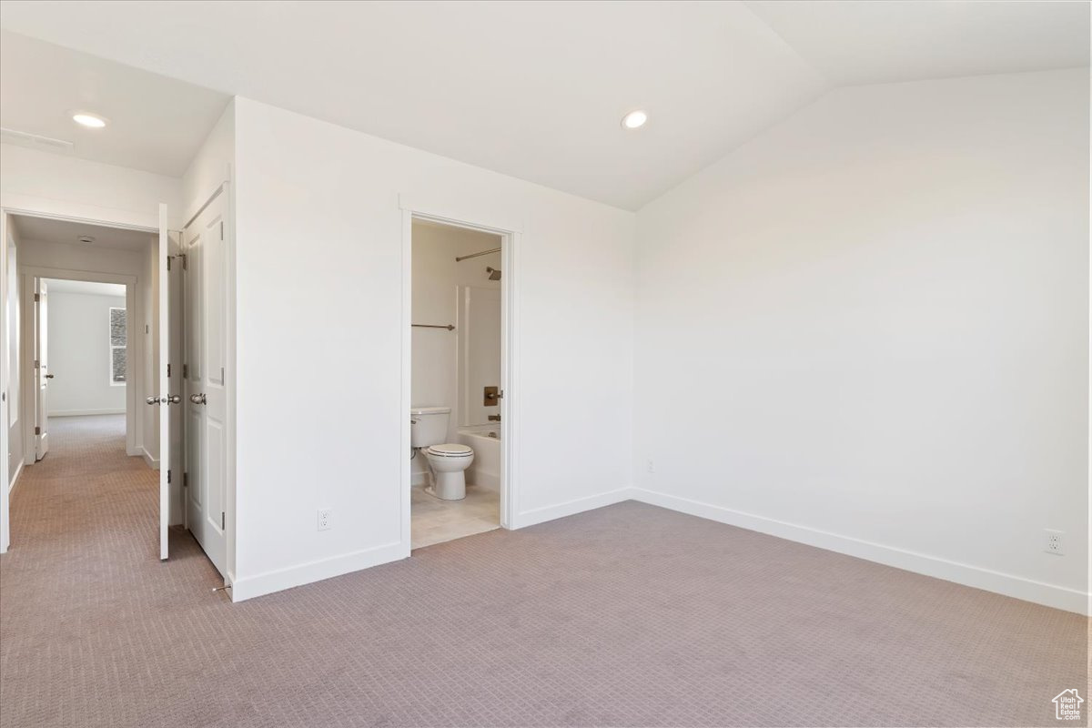 Unfurnished bedroom featuring lofted ceiling, light carpet, and connected bathroom