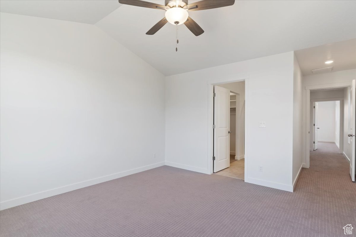 Carpeted spare room with ceiling fan and vaulted ceiling