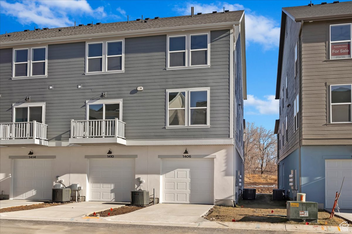 Rear view of property featuring cooling unit, a garage, and a balcony