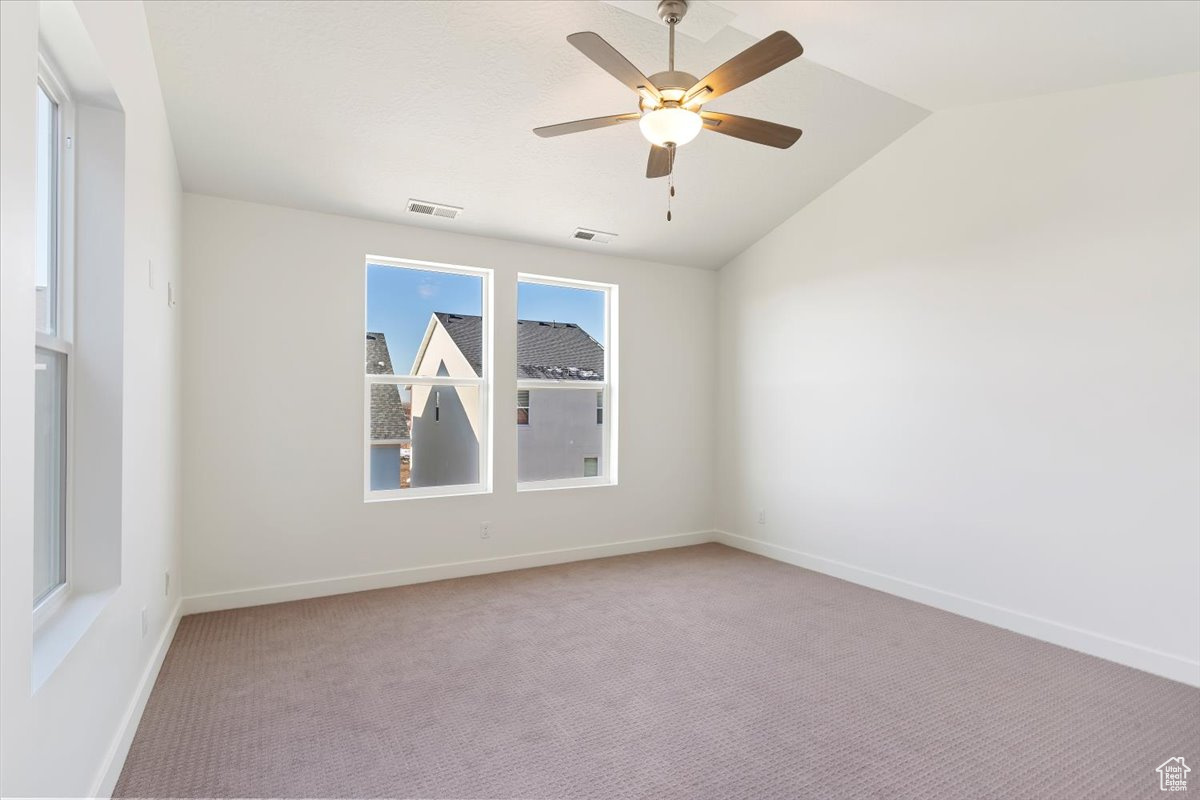 Carpeted spare room with ceiling fan and vaulted ceiling