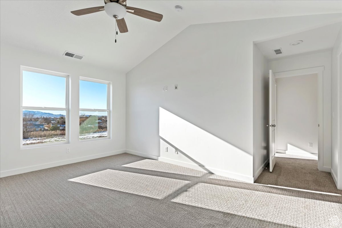 Unfurnished room with dark colored carpet, ceiling fan, and lofted ceiling