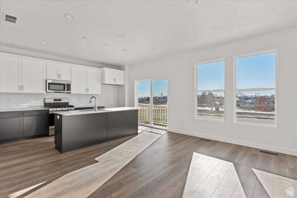 Kitchen featuring backsplash, hardwood / wood-style flooring, an island with sink, white cabinetry, and stainless steel appliances