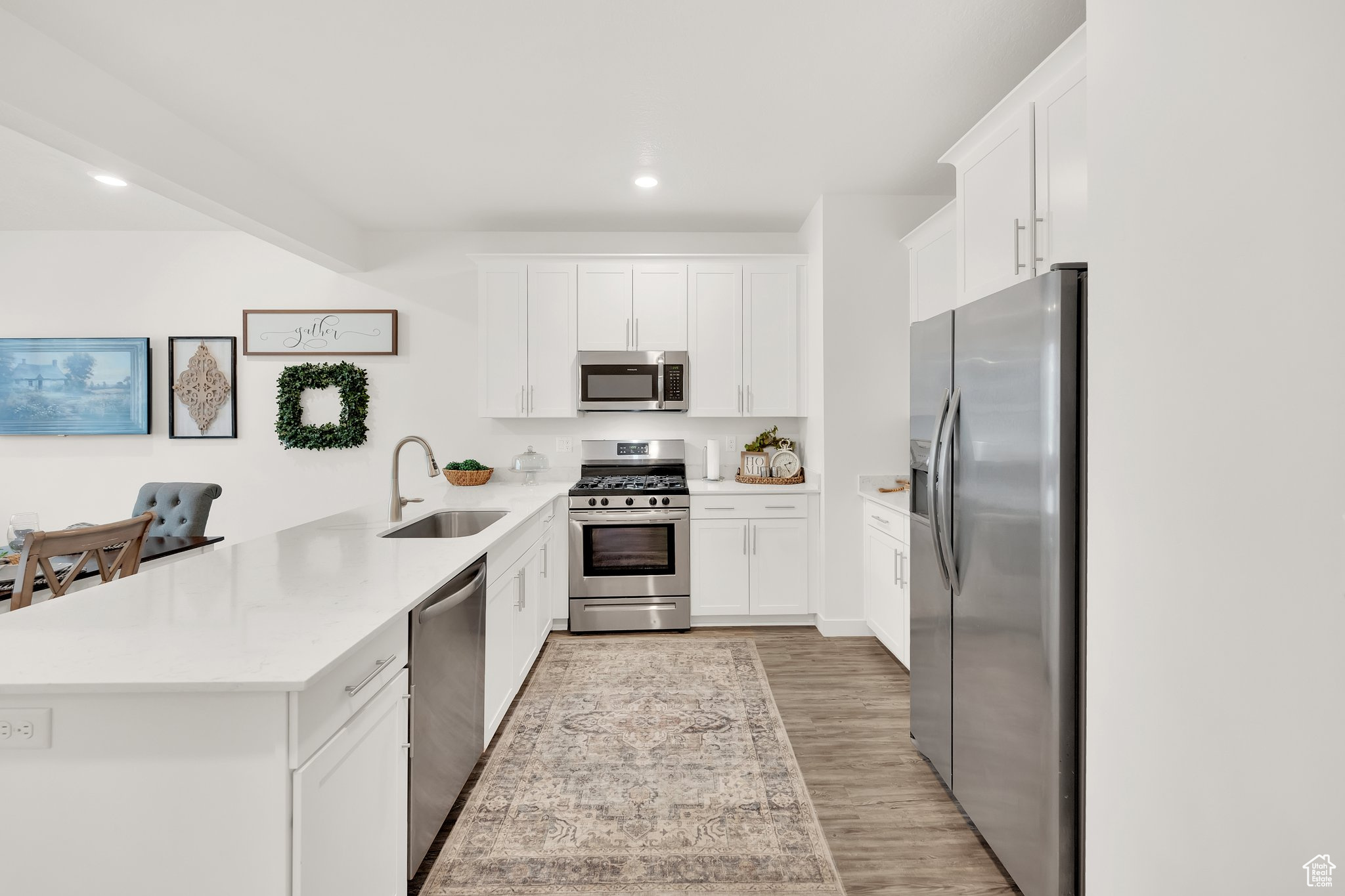 Kitchen with white cabinets, sink, light hardwood / wood-style floors, kitchen peninsula, and stainless steel appliances