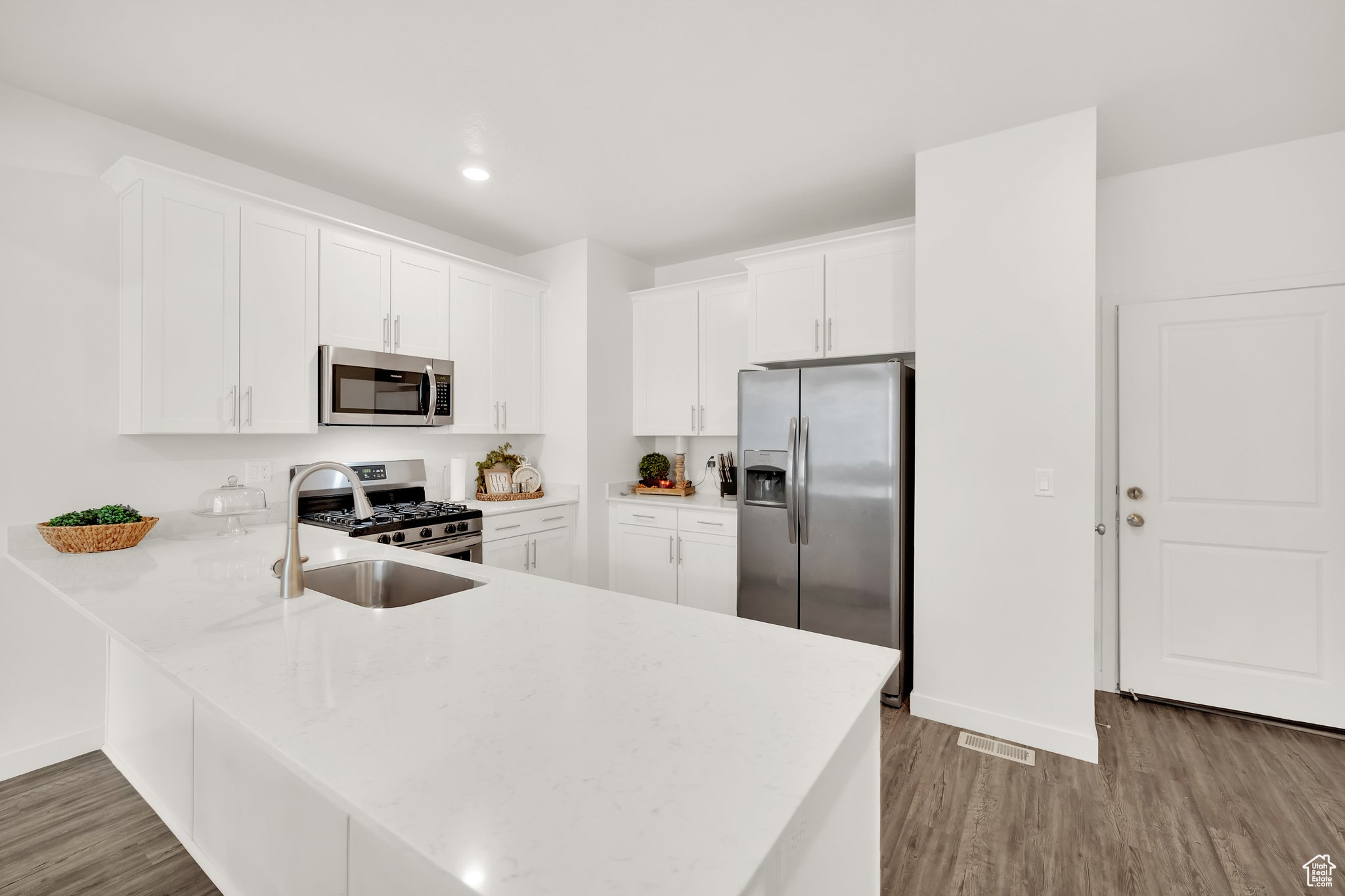 Kitchen featuring kitchen peninsula, appliances with stainless steel finishes, dark hardwood / wood-style flooring, sink, and white cabinets