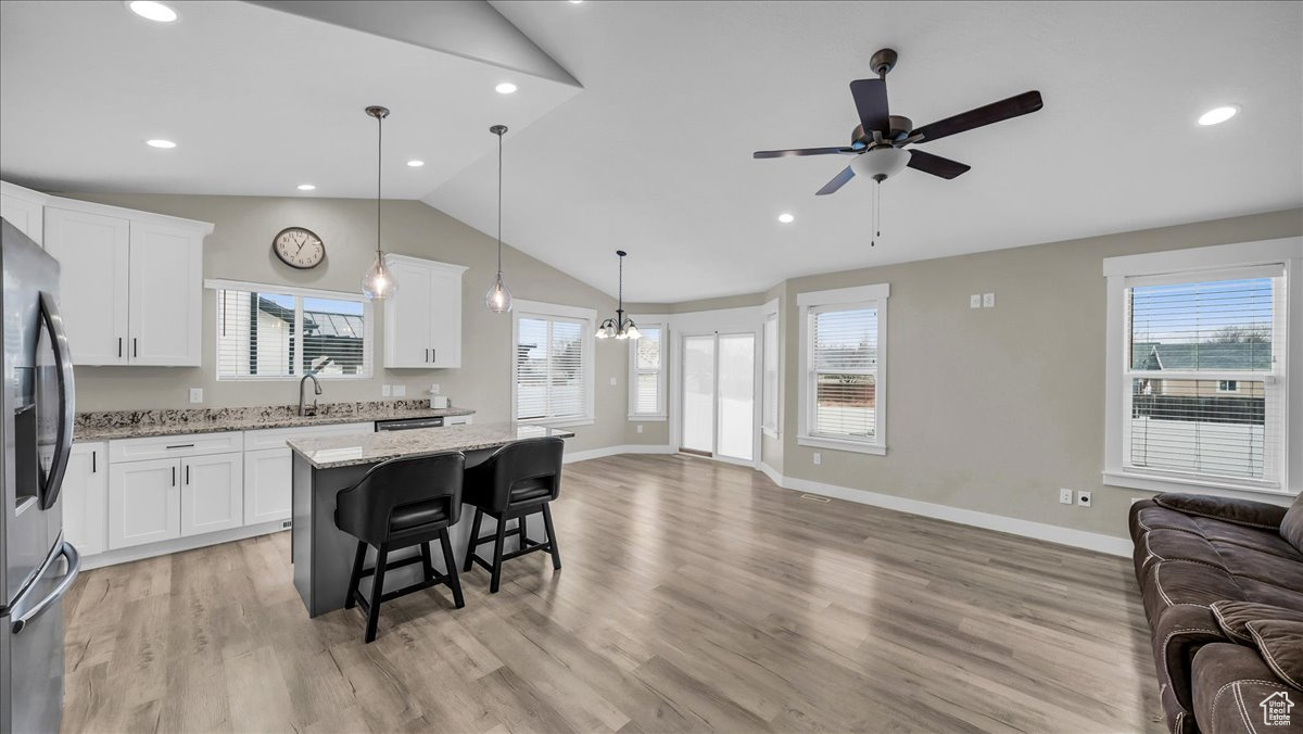 Kitchen with light stone countertops, white cabinetry, pendant lighting, a kitchen island, and ceiling fan with notable chandelier