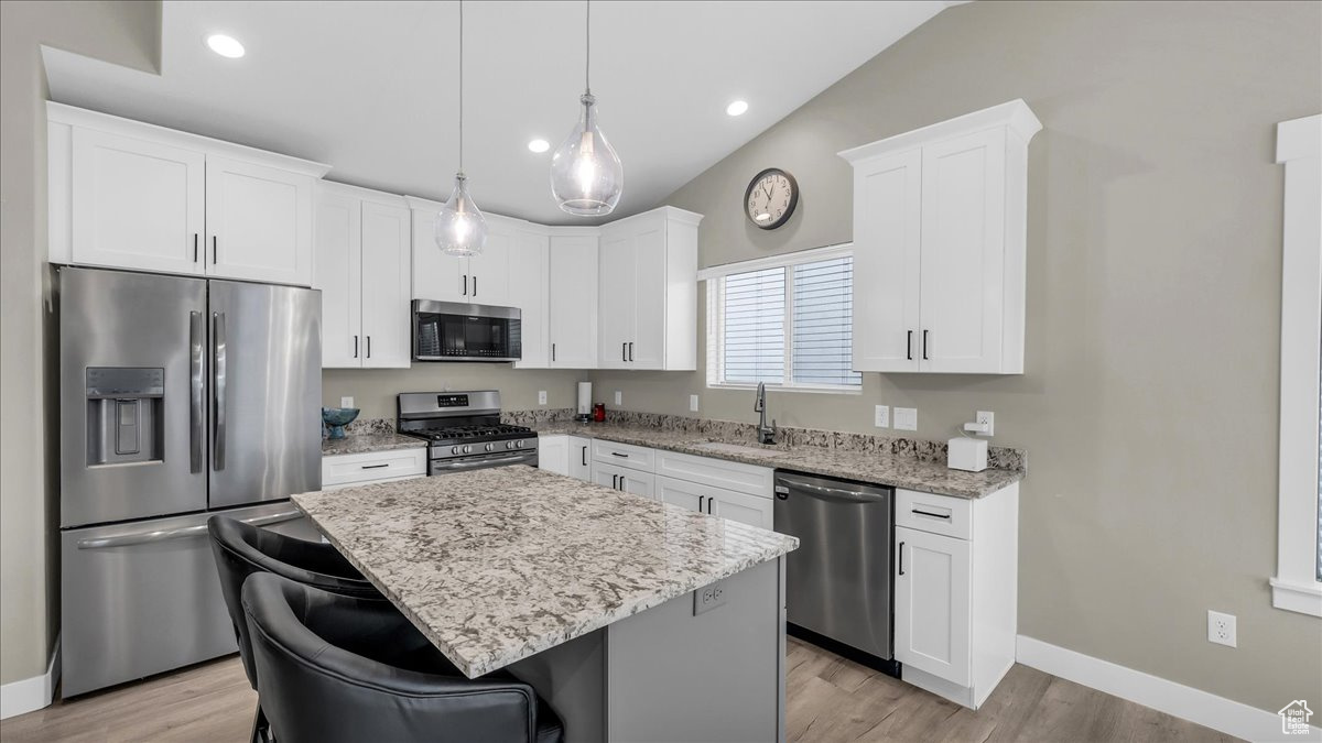 Kitchen featuring pendant lighting, white cabinets, sink, appliances with stainless steel finishes, and a kitchen island