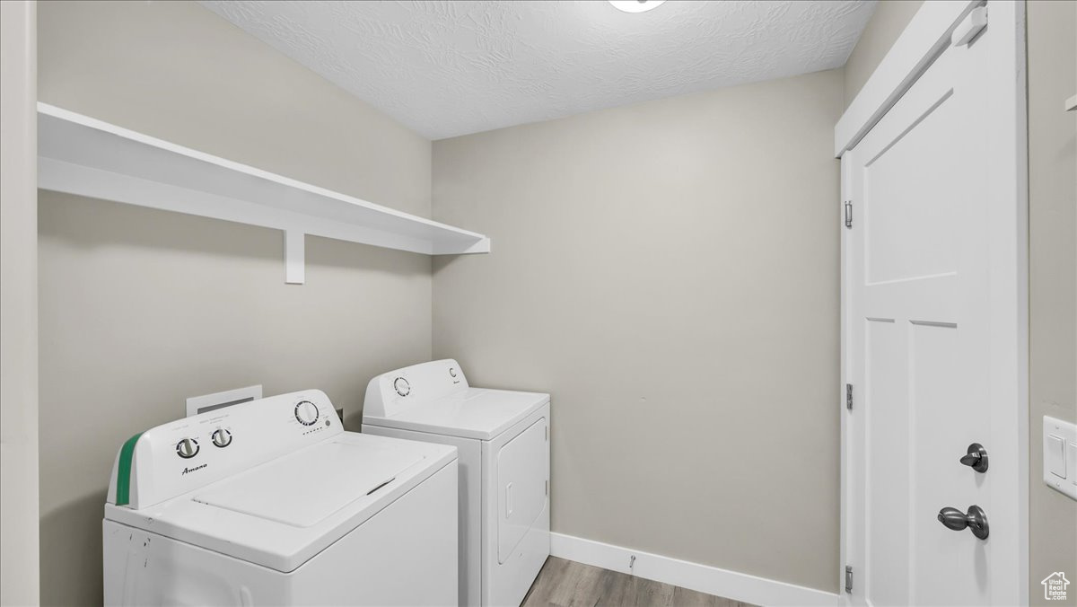 Laundry area featuring a textured ceiling, washing machine and dryer, and light hardwood / wood-style floors