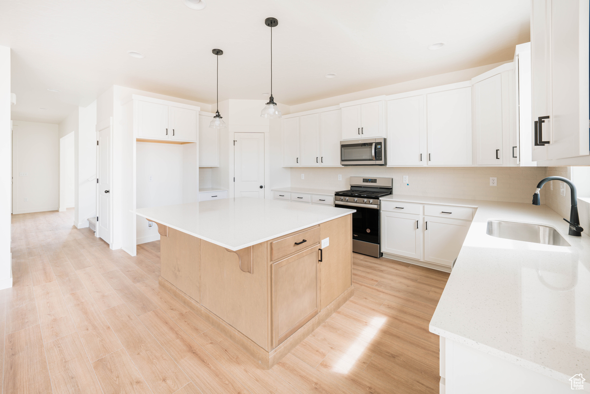 Kitchen with a center island, sink, appliances with stainless steel finishes, decorative light fixtures, and white cabinetry