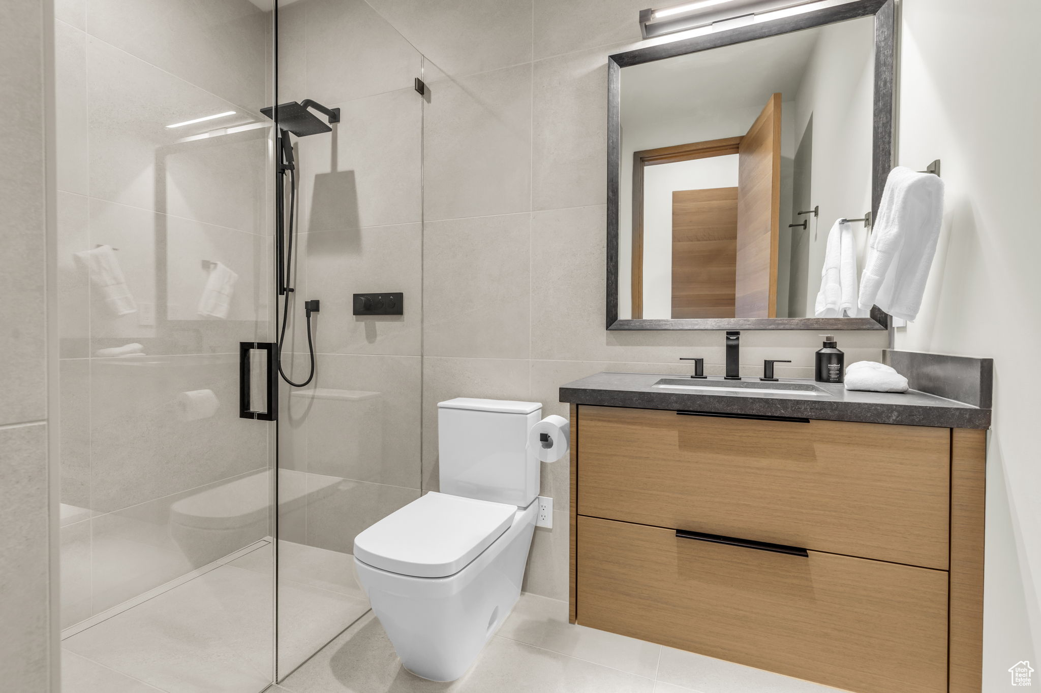 Bathroom featuring vanity, toilet, an enclosed shower, and tile walls