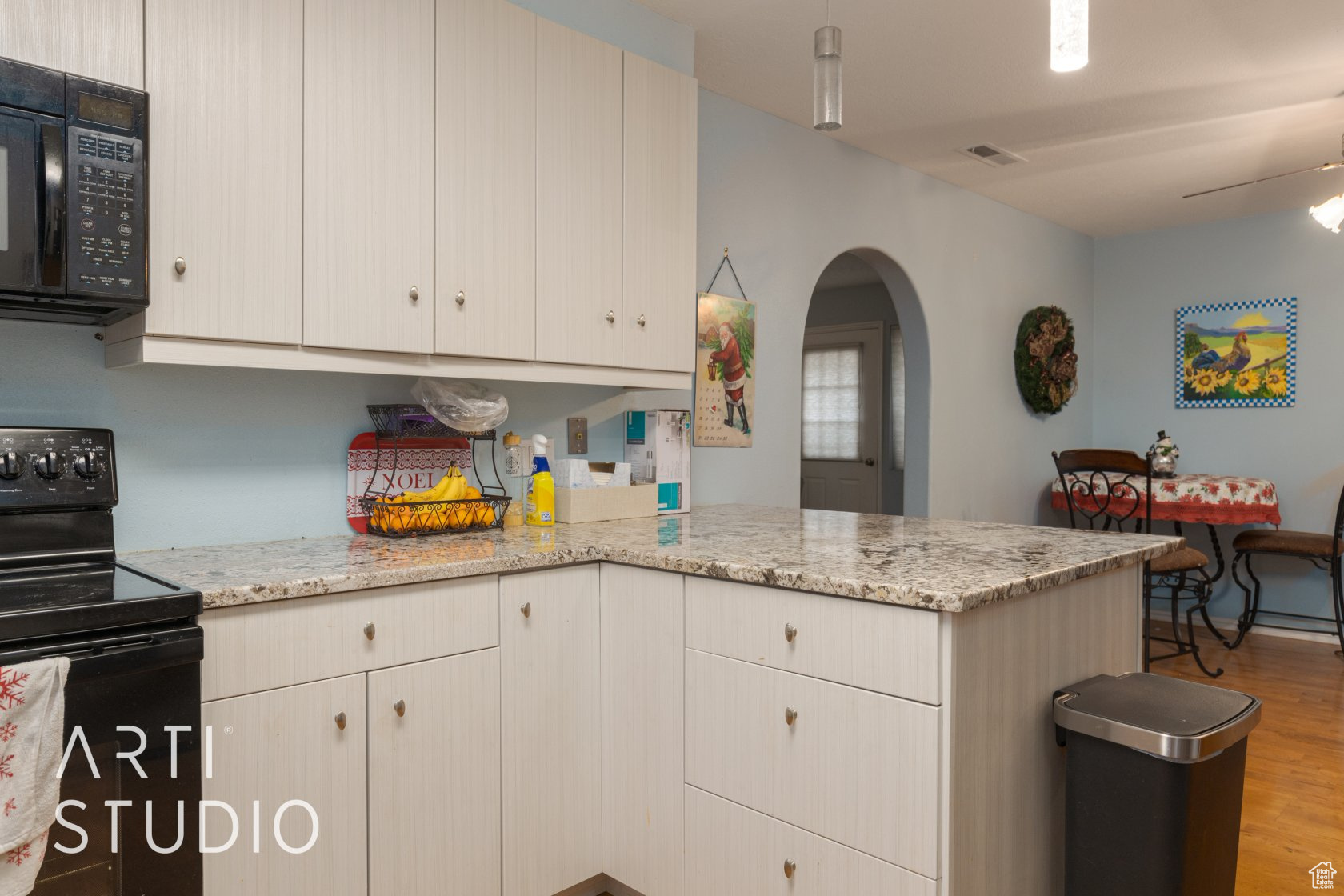 Kitchen featuring kitchen peninsula, light stone counters, ceiling fan, black appliances, and light hardwood / wood-style flooring