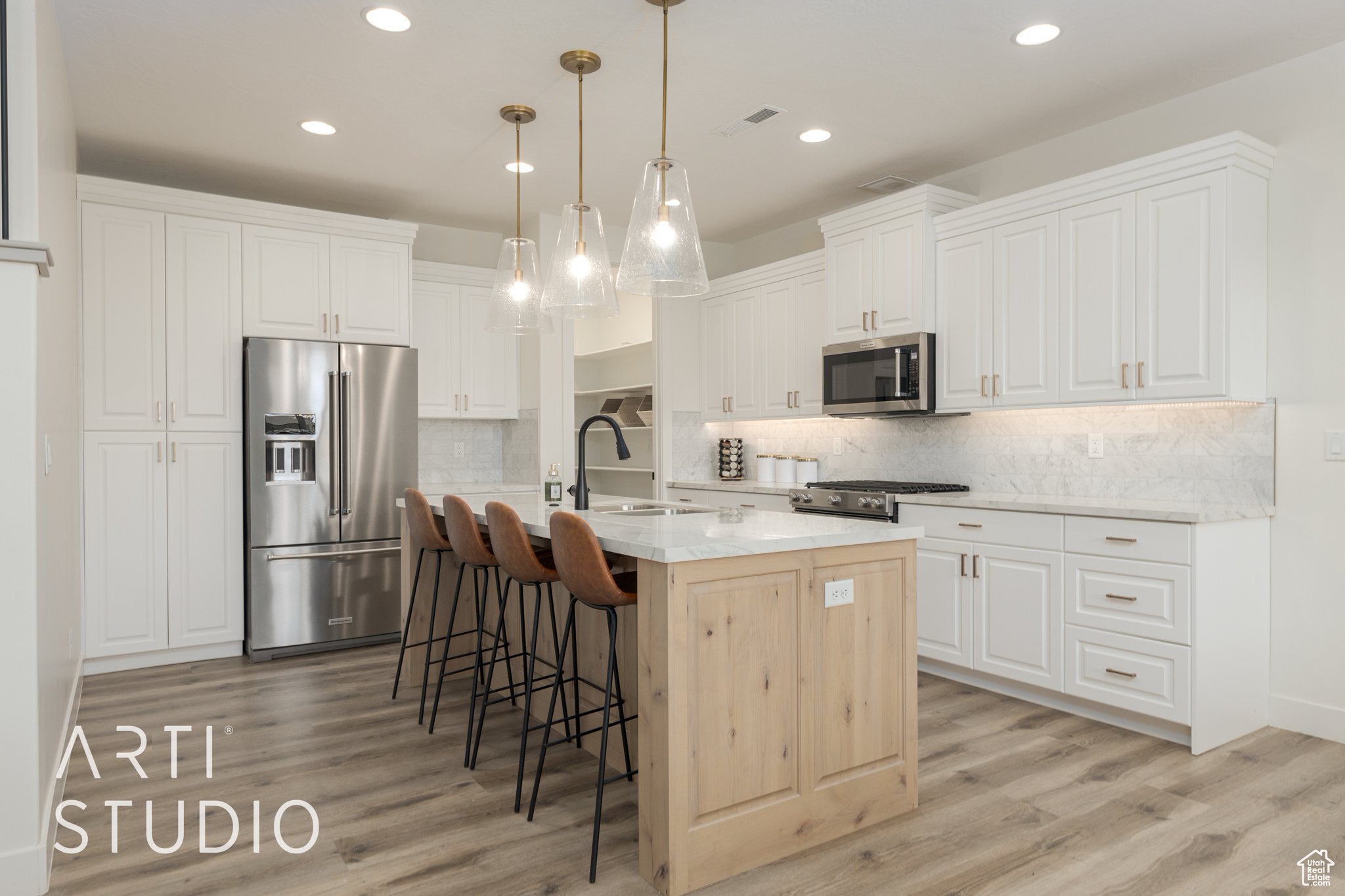 Kitchen featuring a center island with sink, white cabinets, sink, appliances with stainless steel finishes, and decorative light fixtures