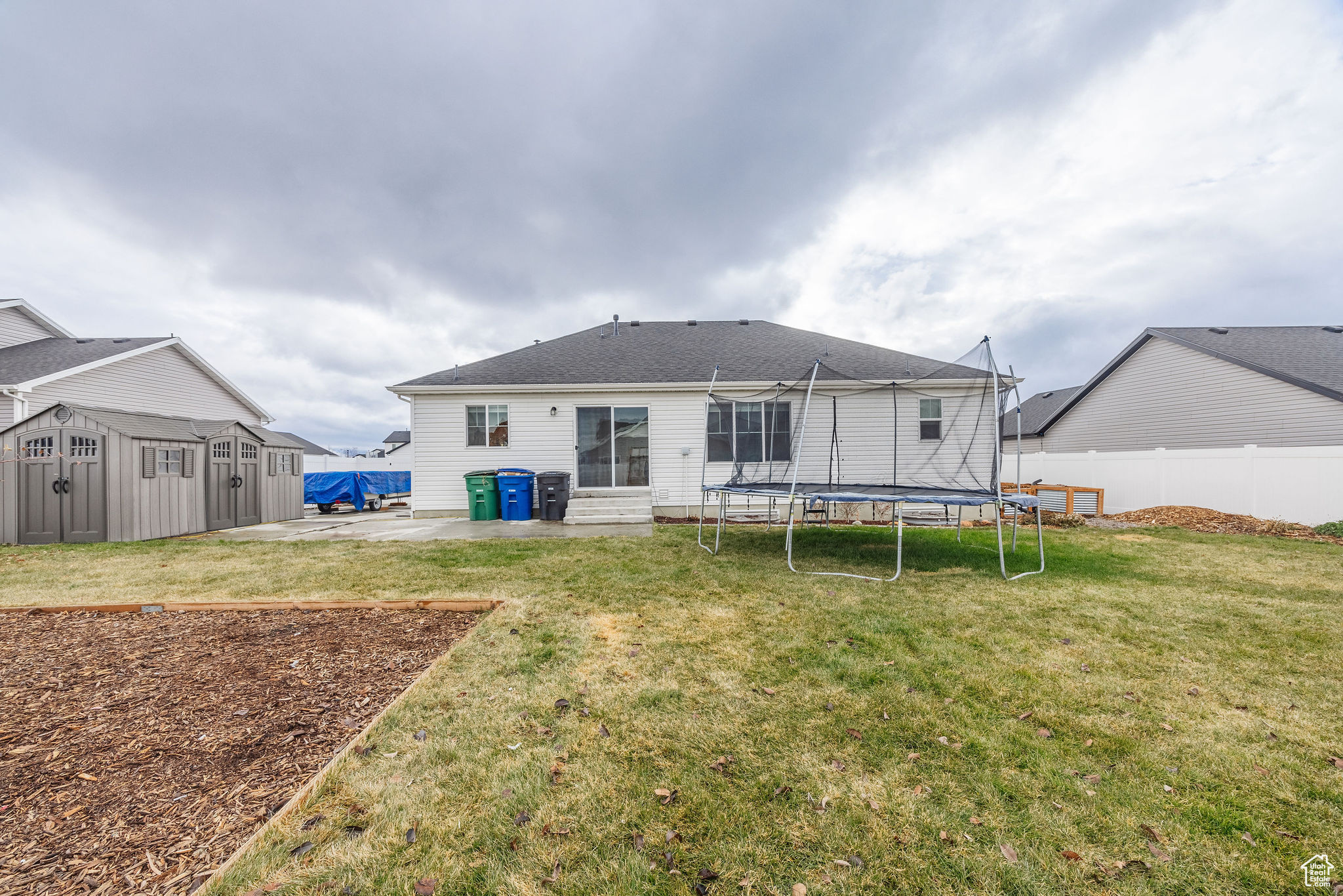 Back of property with a patio area, a yard, a trampoline, and a storage shed