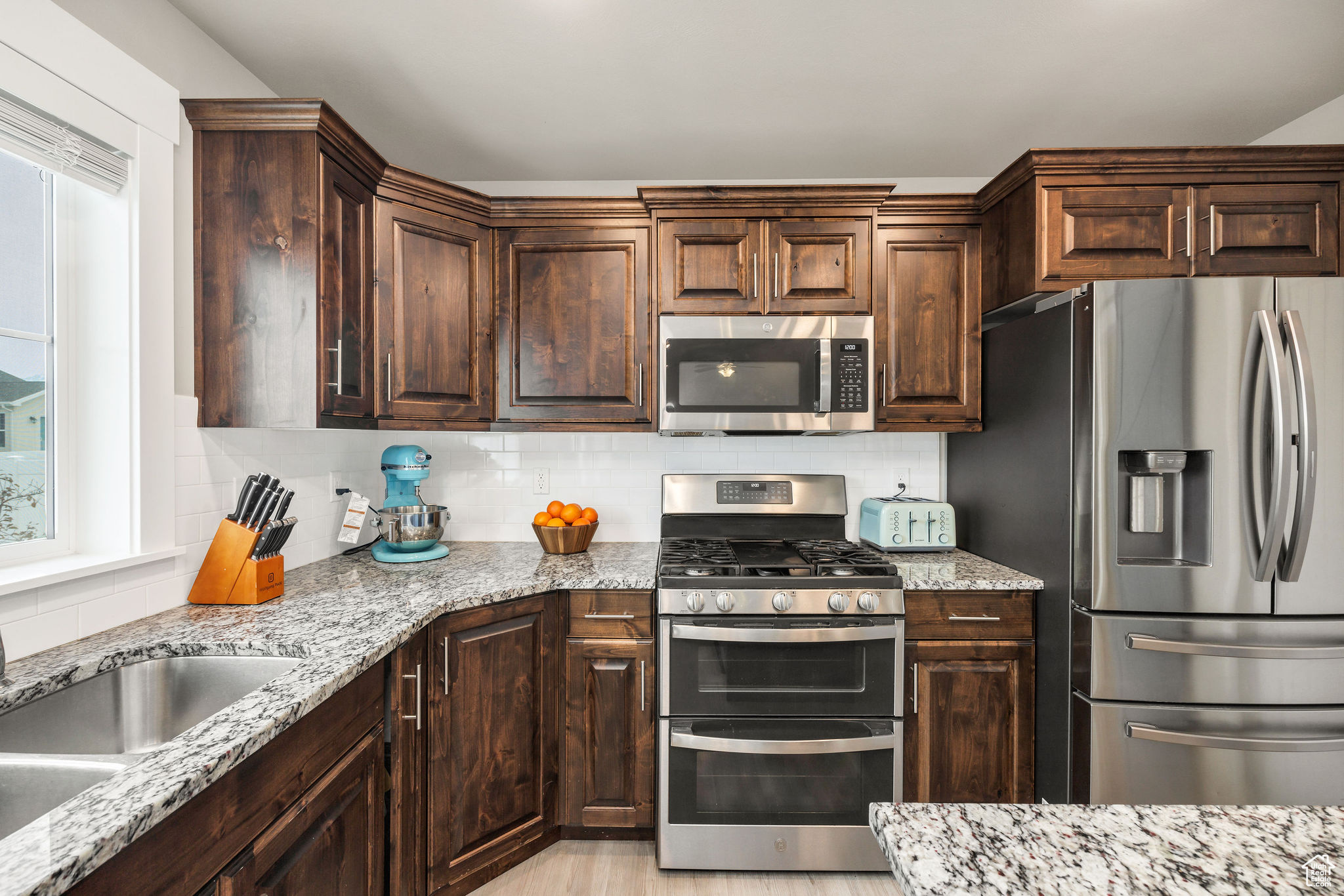 Kitchen with sink, decorative backsplash, light stone countertops, dark brown cabinets, and stainless steel appliances