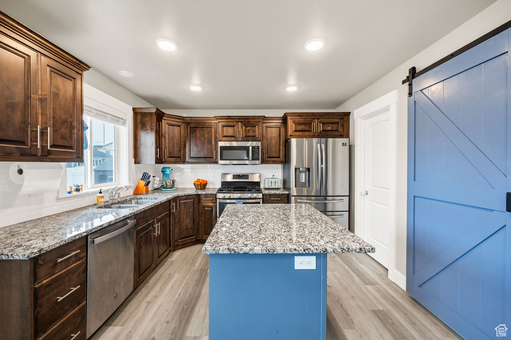 Kitchen with sink, light hardwood / wood-style flooring, a barn door, a kitchen island, and stainless steel appliances